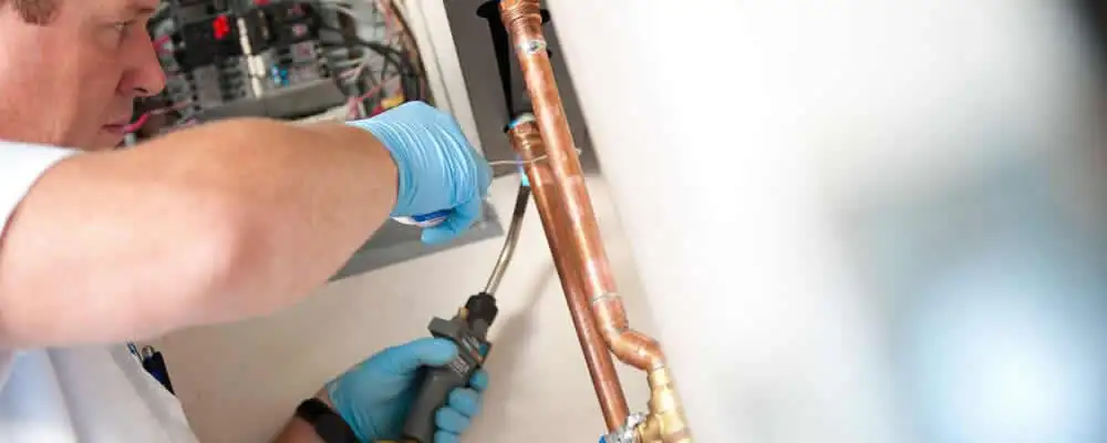 Water heater repair technician testing copper pipe connections and controls in Madison, WI